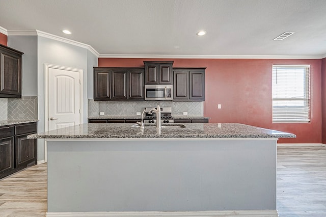 kitchen featuring sink, light stone counters, light wood-type flooring, and an island with sink