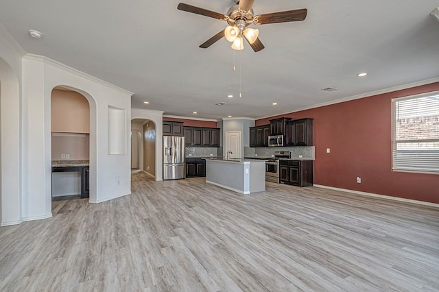 kitchen with appliances with stainless steel finishes, an island with sink, ornamental molding, light hardwood / wood-style flooring, and dark brown cabinets