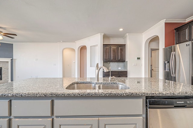 kitchen with dark brown cabinetry, stainless steel appliances, a fireplace, sink, and light stone counters