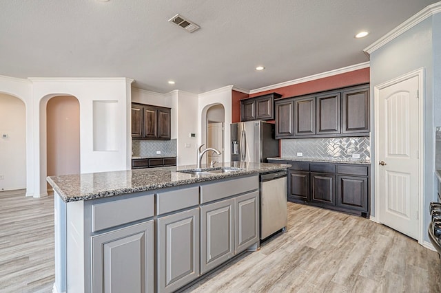 kitchen with sink, appliances with stainless steel finishes, a kitchen island with sink, and tasteful backsplash