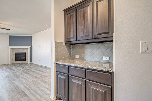 kitchen featuring light stone counters, dark brown cabinetry, ornamental molding, and tasteful backsplash