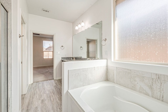 bathroom featuring sink, hardwood / wood-style floors, and a relaxing tiled tub