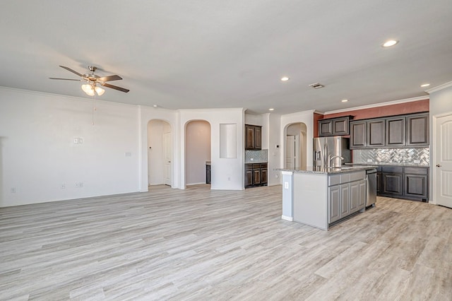 kitchen with stainless steel appliances, an island with sink, ornamental molding, and tasteful backsplash