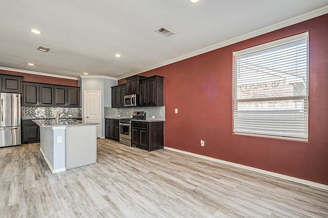 kitchen featuring appliances with stainless steel finishes, tasteful backsplash, sink, light hardwood / wood-style flooring, and an island with sink