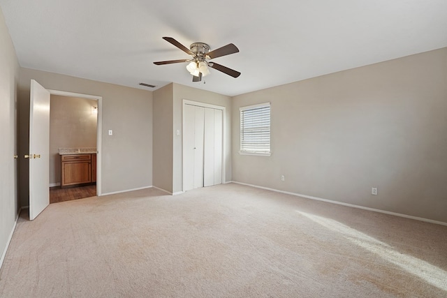 unfurnished bedroom with connected bathroom, light colored carpet, ceiling fan, and a closet