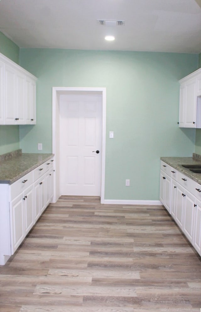 kitchen featuring light stone counters, white cabinets, and light wood-type flooring