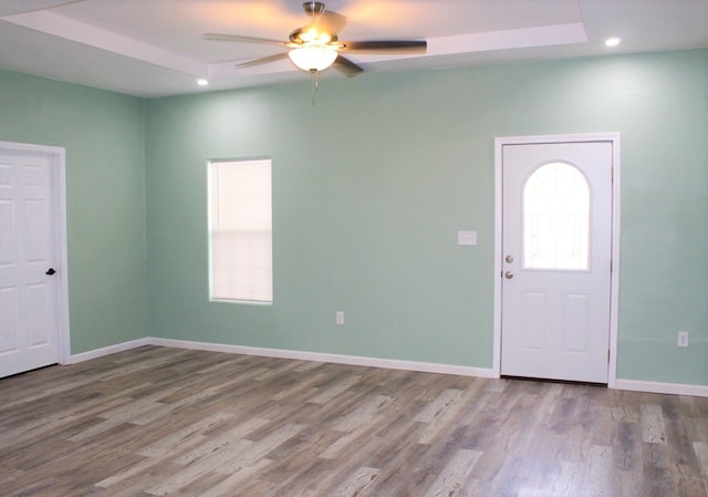 foyer entrance with ceiling fan, a raised ceiling, and wood-type flooring