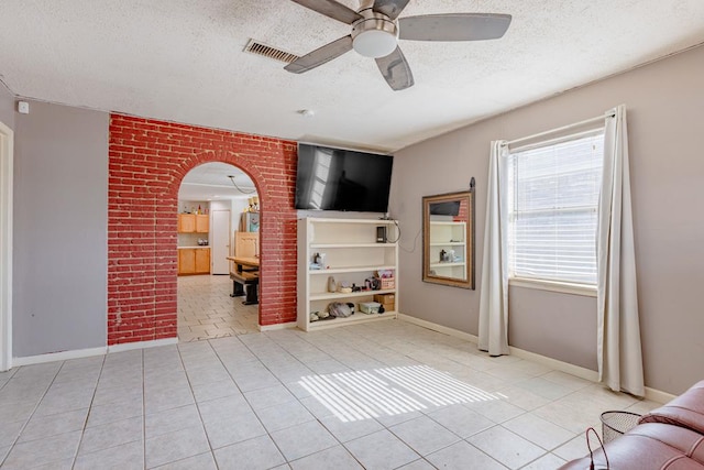 1304 Lynn Ave, Midland, TX 79705 - unfurnished living room featuring a textured ceiling, tile patterned floors, a ceiling fan, arched walkways, and baseboards