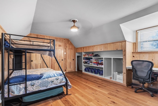 bedroom featuring ceiling fan, wood walls, light hardwood / wood-style flooring, and vaulted ceiling