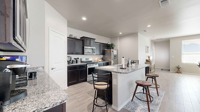 kitchen with light stone counters, light hardwood / wood-style flooring, stainless steel appliances, and a breakfast bar area