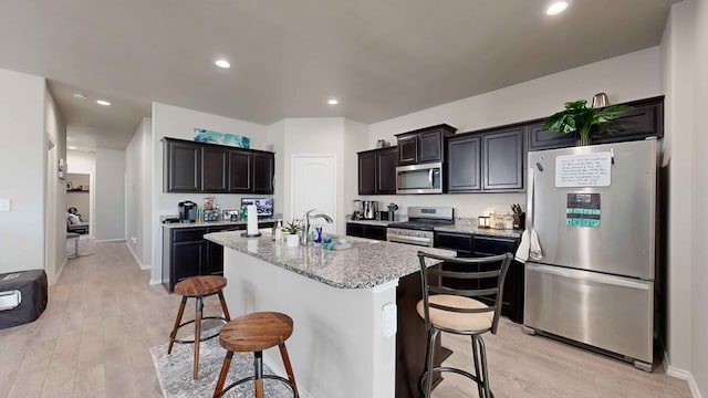 kitchen featuring a kitchen breakfast bar, an island with sink, light stone countertops, and appliances with stainless steel finishes