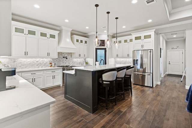 3100 Fairfield Ln, Midland, TX 79705 - kitchen featuring appliances with stainless steel finishes, custom range hood, a kitchen island with sink, white cabinets, and backsplash