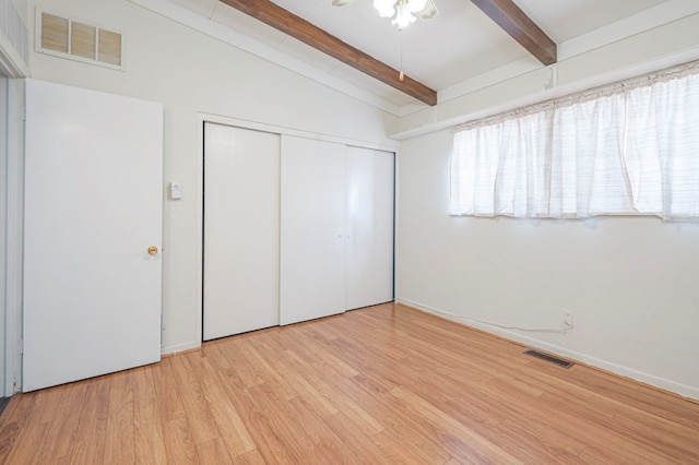 unfurnished bedroom with lofted ceiling with beams, light wood-type flooring, and a closet