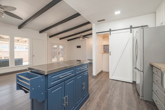 kitchen with dark wood-type flooring, blue cabinets, stainless steel fridge, ceiling fan, and a barn door