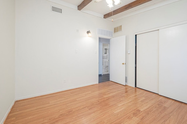 unfurnished bedroom with ceiling fan, light hardwood / wood-style floors, a closet, and beamed ceiling