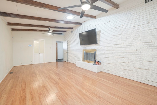 unfurnished living room featuring light hardwood / wood-style flooring, beamed ceiling, ceiling fan, and brick wall