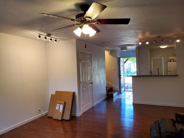 empty room with a textured ceiling, ceiling fan, rail lighting, and dark hardwood / wood-style floors