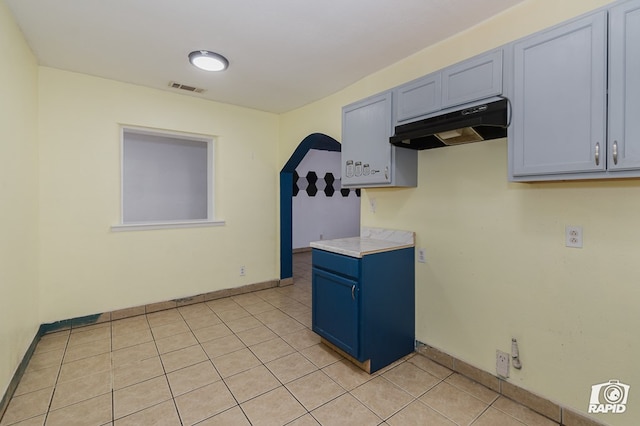 111 W Pine Ave, Midland, TX 79705 - kitchen with under cabinet range hood, light tile patterned flooring, light countertops, blue cabinets, and arched walkways