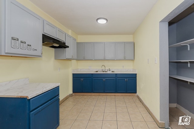 111 W Pine Ave, Midland, TX 79705 - kitchen with under cabinet range hood, blue cabinetry, light tile patterned flooring, and light countertops