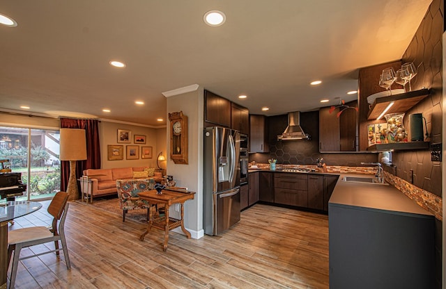 kitchen with wall chimney range hood, sink, light hardwood / wood-style flooring, ornamental molding, and stainless steel appliances