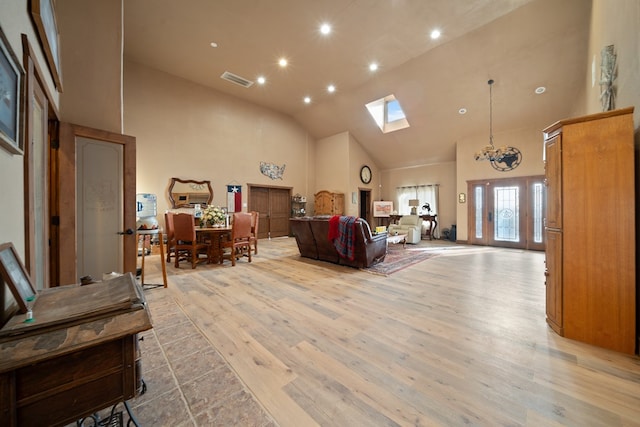 living room featuring a chandelier, light wood-type flooring, high vaulted ceiling, and a skylight