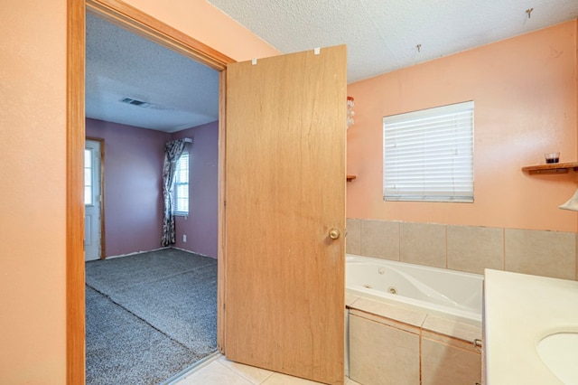 bathroom with tile patterned flooring, vanity, a textured ceiling, and tiled tub