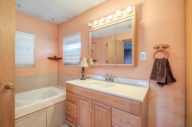 bathroom with vanity, a textured ceiling, and tiled tub