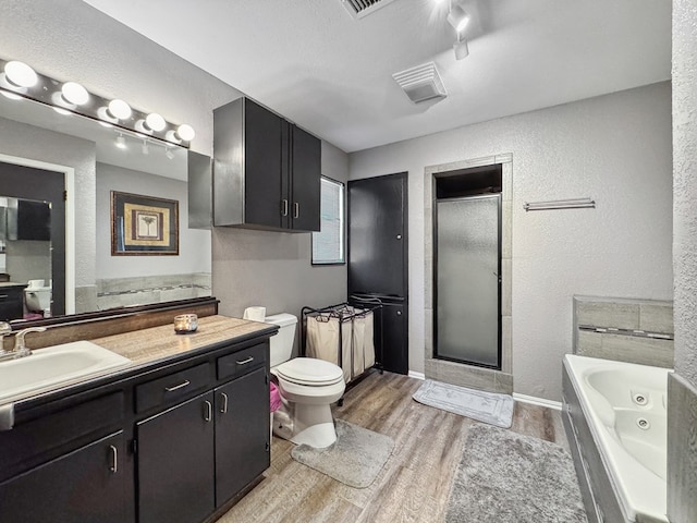 bathroom with toilet, a stall shower, vanity, wood finished floors, and a tub with jets