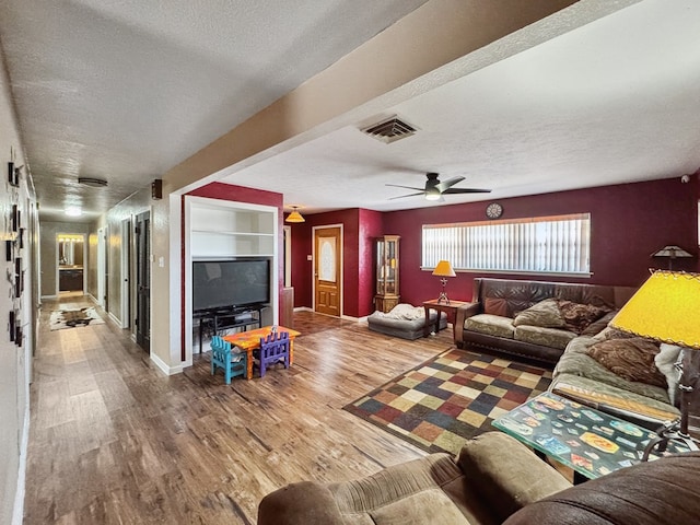 living area featuring built in features, visible vents, a textured ceiling, wood finished floors, and baseboards