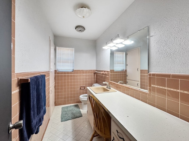 bathroom with tile walls, toilet, wainscoting, vanity, and tile patterned flooring