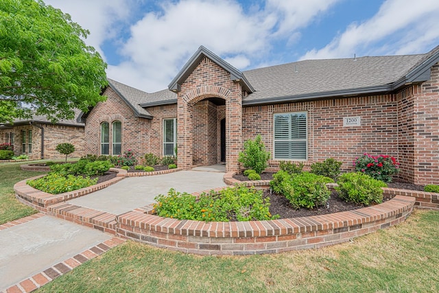 view of front of home with brick siding, a shingled roof, and a front lawn