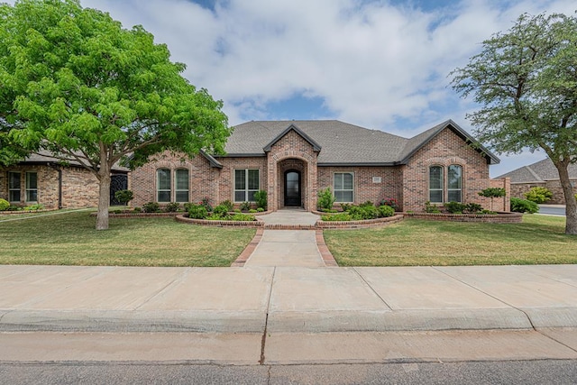 view of front of house with brick siding, a front lawn, and a shingled roof