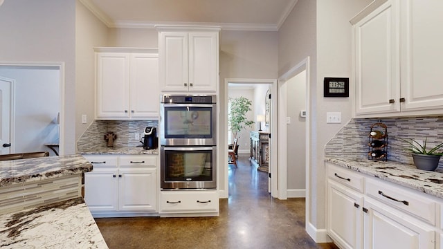 kitchen with double oven, backsplash, finished concrete floors, white cabinets, and light stone counters