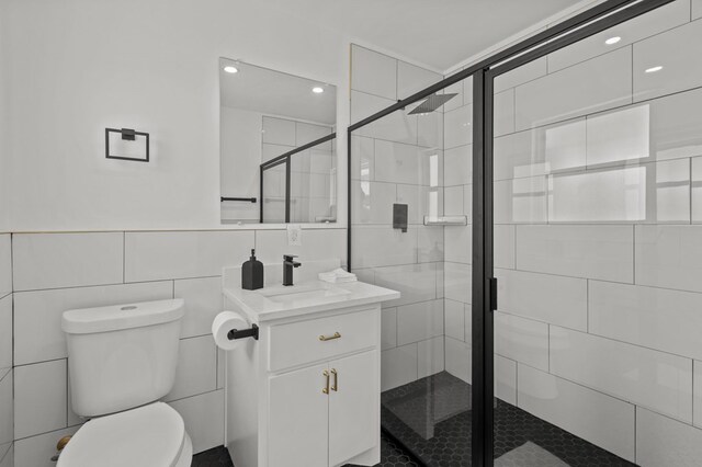 bathroom featuring vanity, toilet, a shower with door, and tile walls