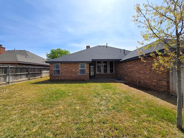 rear view of property featuring a chimney, a lawn, brick siding, a fenced backyard, and a shingled roof