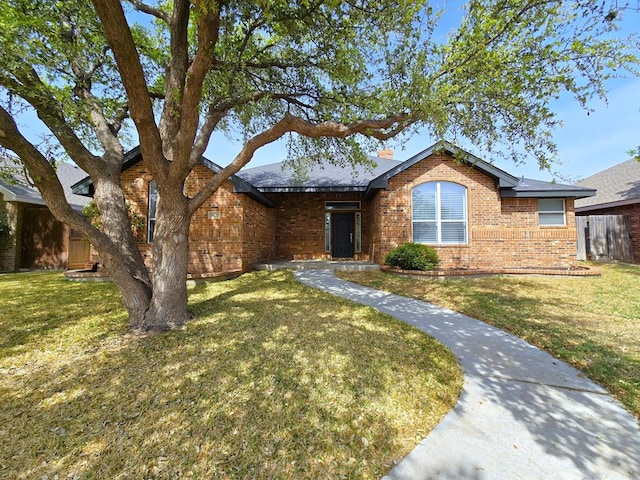 single story home with a chimney, a front lawn, and brick siding