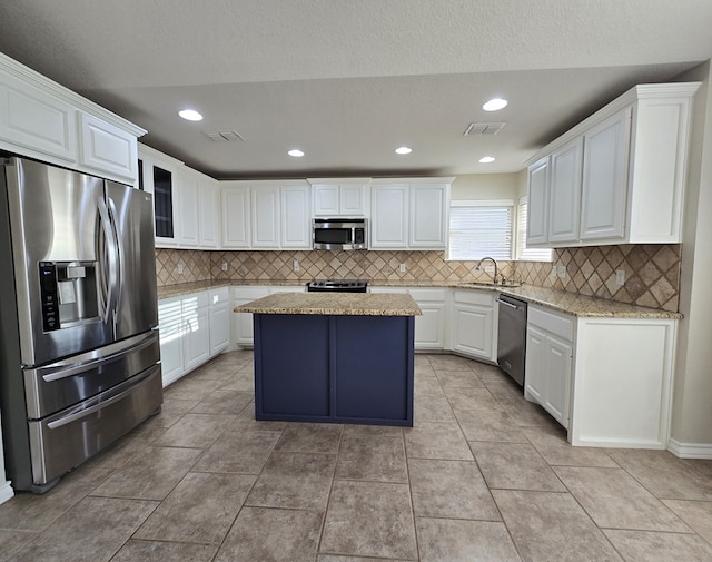 kitchen with stainless steel appliances, white cabinetry, decorative backsplash, a kitchen island, and visible vents