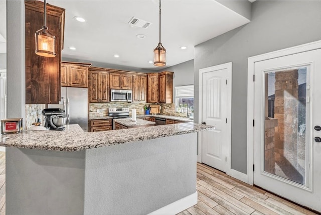 kitchen with pendant lighting, backsplash, stainless steel appliances, light stone countertops, and kitchen peninsula