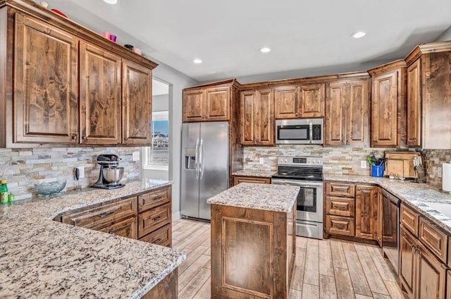 kitchen featuring light stone counters, stainless steel appliances, a kitchen island, and light hardwood / wood-style flooring