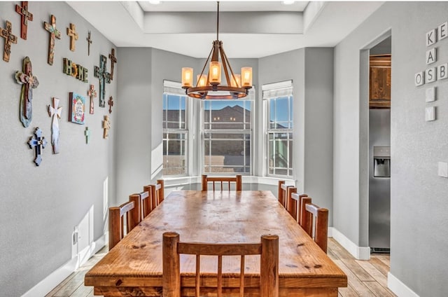 dining space with plenty of natural light, light hardwood / wood-style floors, a raised ceiling, and a chandelier