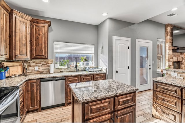 kitchen featuring light stone counters, a center island, stainless steel appliances, a fireplace, and decorative backsplash