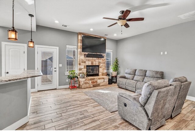 living room featuring ceiling fan, a stone fireplace, and light hardwood / wood-style floors