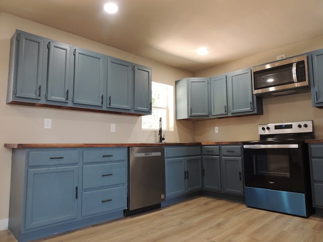 kitchen featuring butcher block countertops, sink, blue cabinetry, stainless steel appliances, and light hardwood / wood-style floors