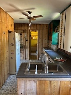 kitchen featuring ceiling fan, wood walls, kitchen peninsula, and sink