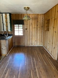 unfurnished dining area with dark hardwood / wood-style floors, sink, and wooden walls