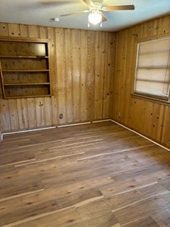 spare room with hardwood / wood-style floors, ceiling fan, built in features, and wooden walls