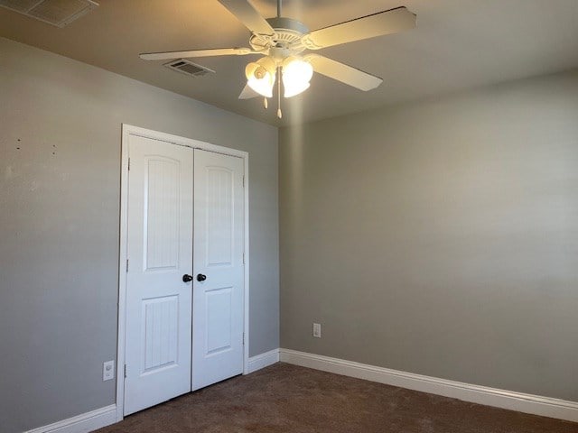 unfurnished bedroom featuring dark colored carpet, a closet, visible vents, and baseboards