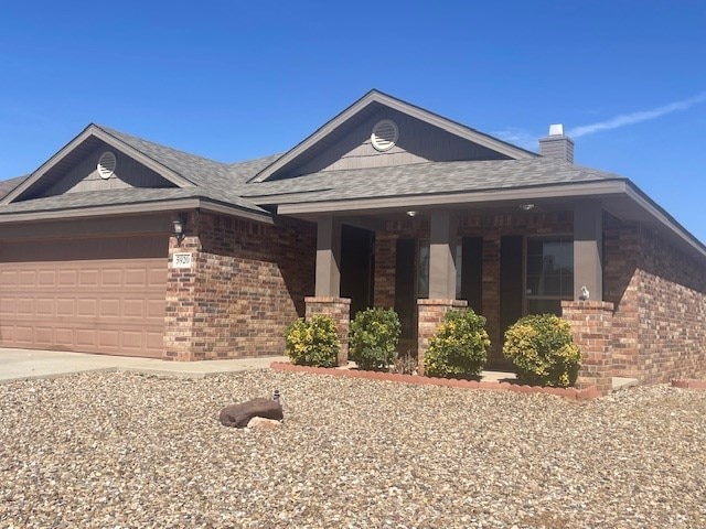 view of front of house featuring brick siding, a chimney, a shingled roof, a garage, and driveway