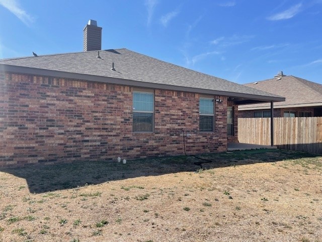 rear view of property with roof with shingles, a chimney, fence, and brick siding