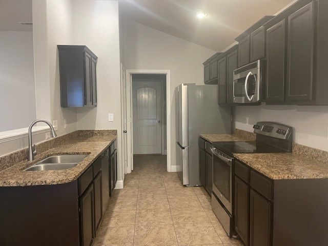 kitchen featuring lofted ceiling, appliances with stainless steel finishes, light tile patterned flooring, a sink, and dark stone counters